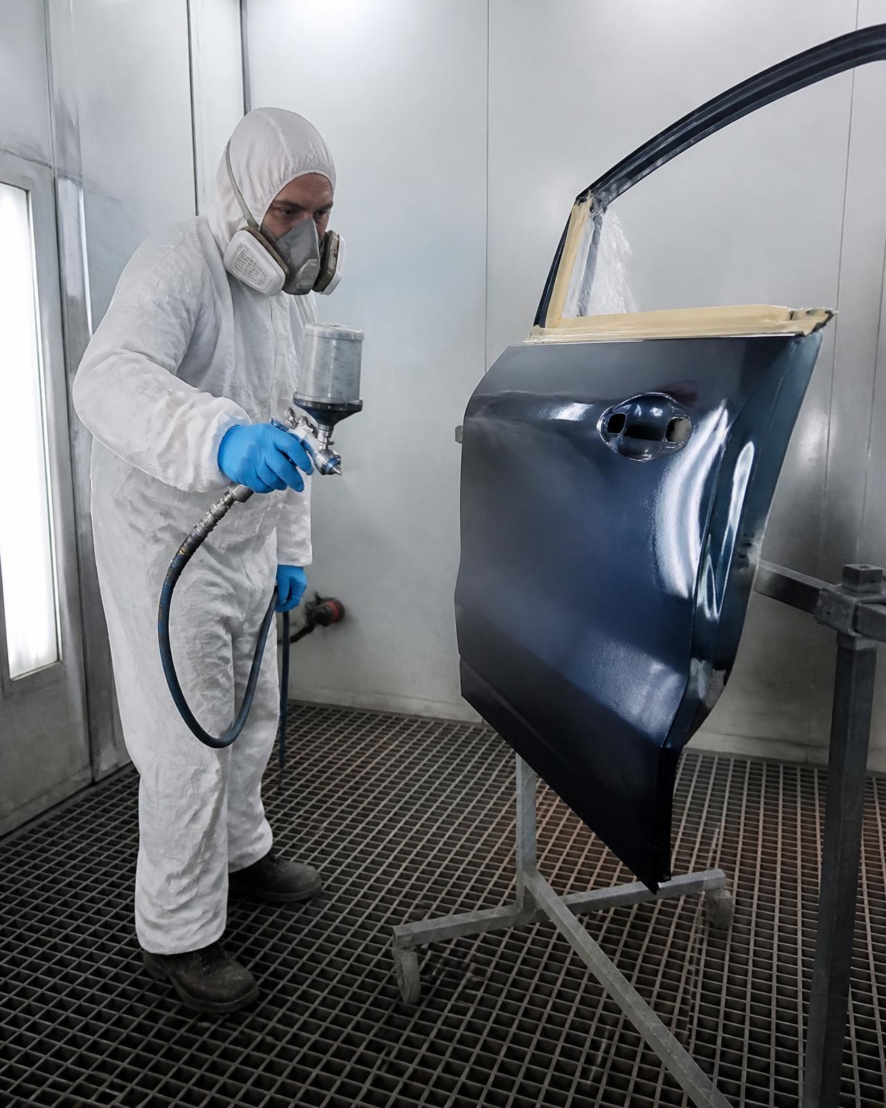 Painter spraying a car door in the booth at Two Brothers Auto Body